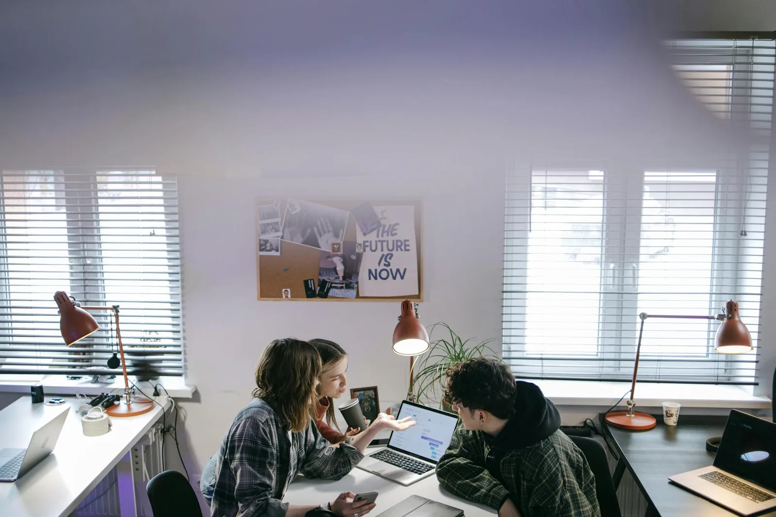 Groupe de personnes discutant d'idées autour d'ordinateurs portables dans un bureau lumineux et moderne
